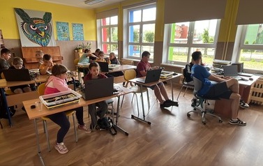 Grupa uczni&oacute;w z SP w Czarnej Dąbr&oacute;wce pracuje przy stolikach, angażując się w zajęcia z robotyki.