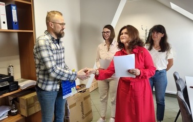 Na zdjęciu w jasnym pomieszczeniu stoją cztery osoby i pozują do zdjęcia. Od lewej strony: Pan Wojciech Jabłonowski, Pani Beata Wolska, Dyrektor Centrum Usług społecznych w Czarnej Dąbr&oacute;wce oraz Pani Katarzyna Podolska.  