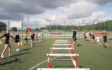 Uczestnicy Akademii Lekkoatletyki wraz z trenerem podczas wykonywania ćwiczeń ruchowych na Orliku w Czarnej Dąbr&oacute;wce.