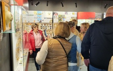 Grupa os&oacute;b ogląda wystawę motyli. W gablotach znajdują się okazy, a na ścianach wiszą tablice informacyjne.