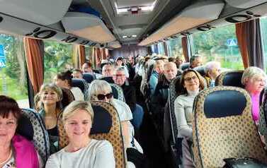 Widok w głąb autokaru wypełnionego pasażerami. Część os&oacute;b patrzy w stronę aparatu i uśmiecha się.