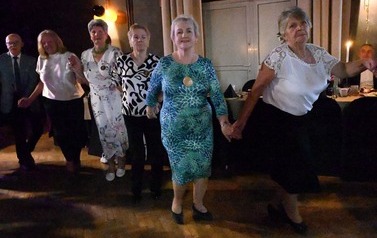 Uczestnicy balu tańczą w kręgu, trzymając się za ręce. 