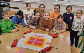 Zdjęcie grupowe uśmiechniętych dzieci biorących udział w zajęciach z kodowania. Prezentują efekt swojej pracy plakat z kodowania.